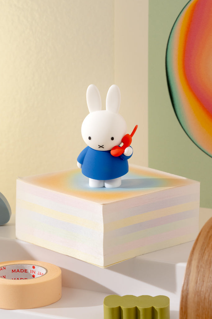 White rabbit figurine in a blue outfit on a colorful block with a red phone