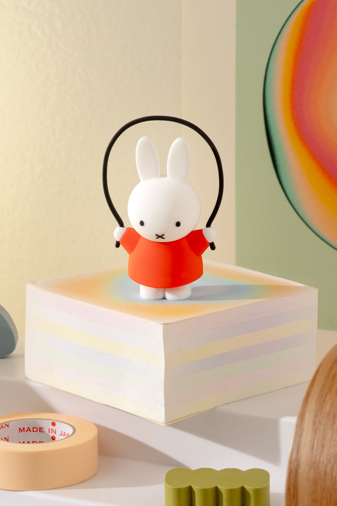 Small rabbit figurine wearing a red outfit on a colorful block with a neutral background