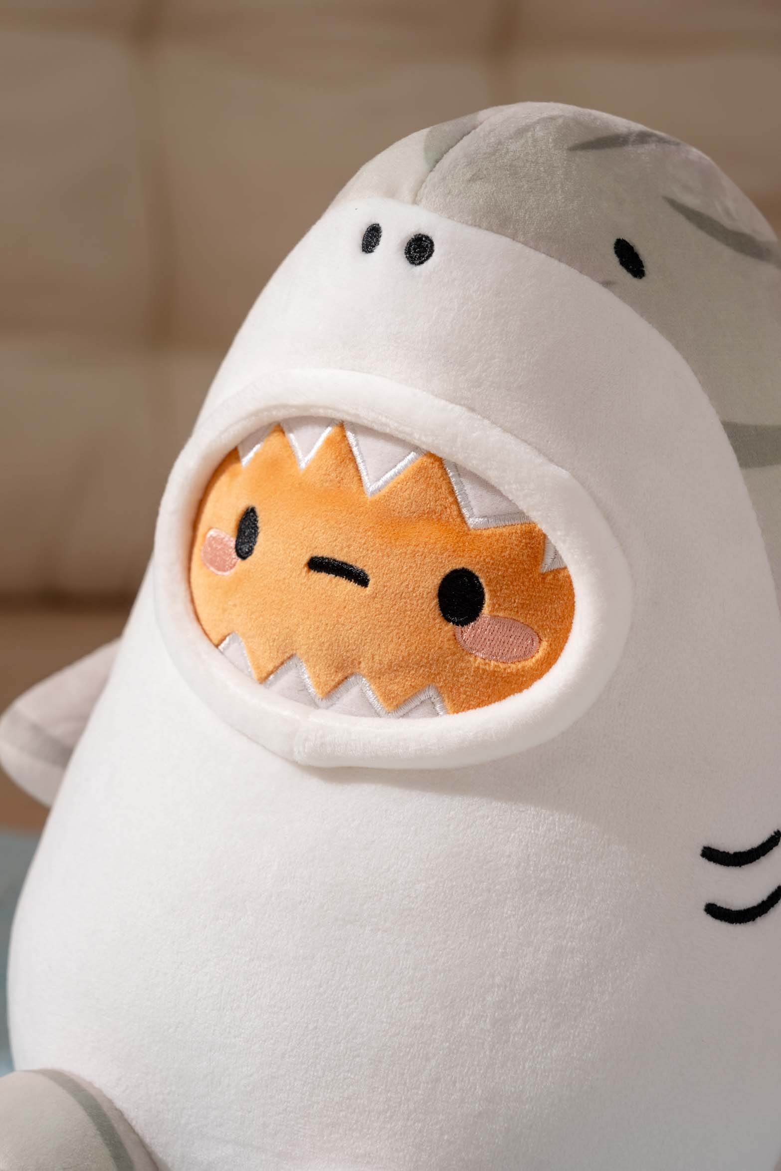 Plush toy of a gray-striped shark eating a frowning orange plush with triangular teeth.
