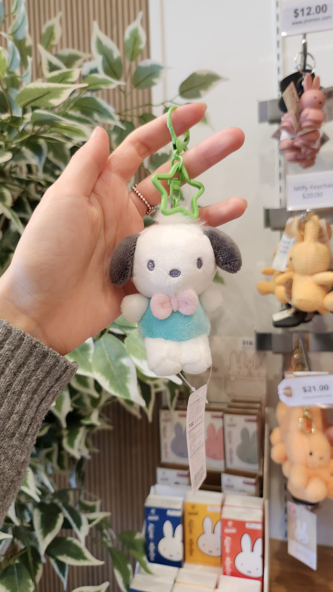 Hand holding a white and gray plush keychain with a light blue shirt and pink bow.