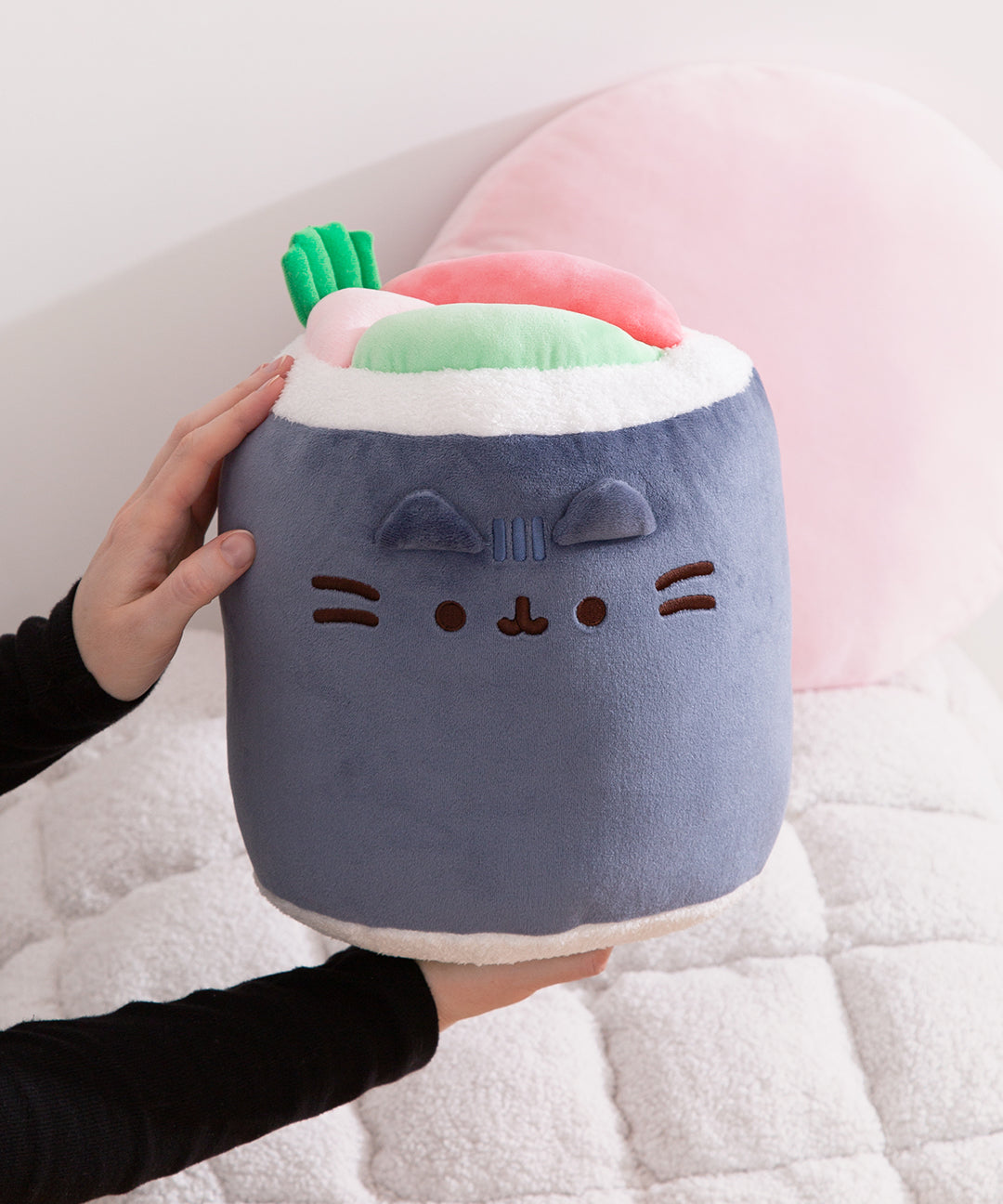 Plush toy shaped like a cat face with a hand holding it on a soft surface