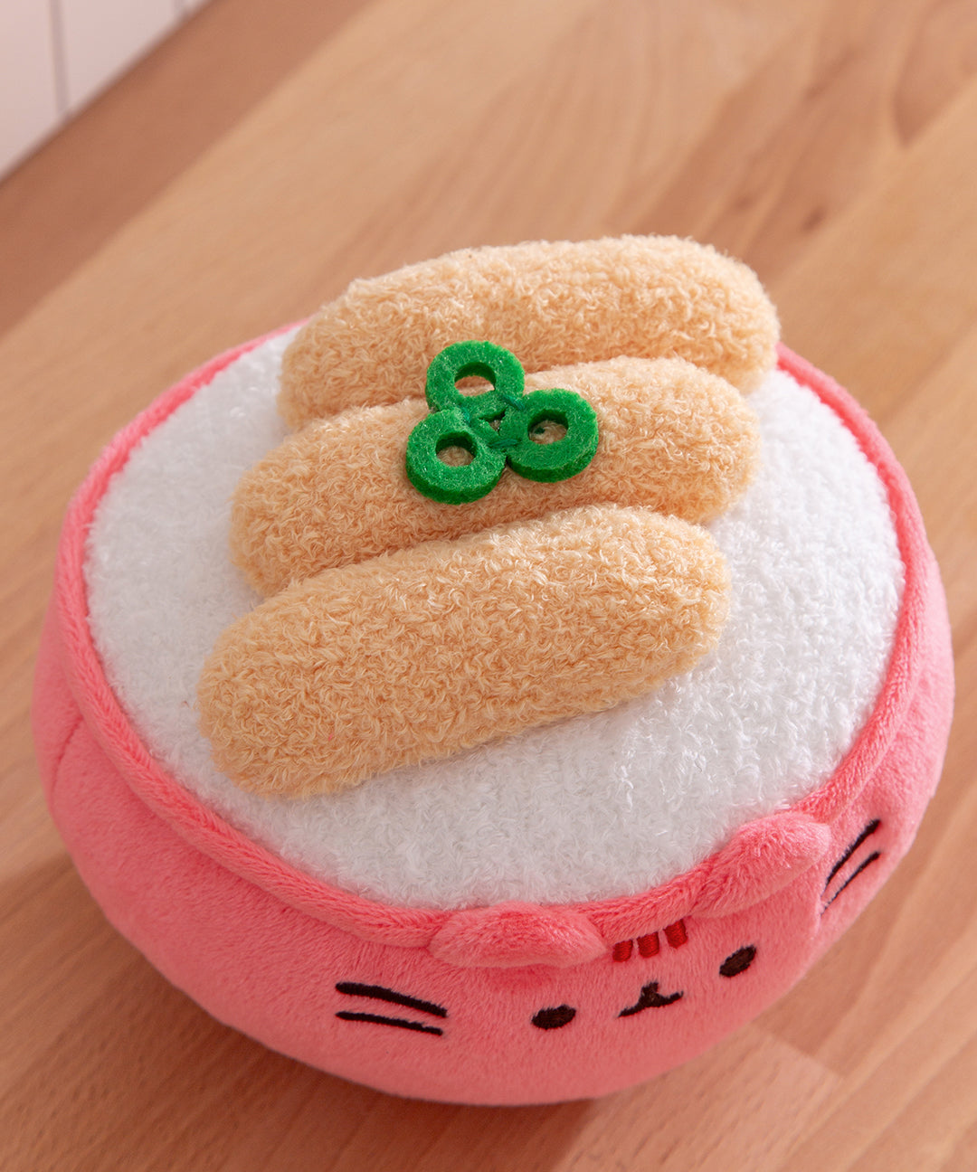 Plush toy resembling a bowl of ramen with noodles on a wooden surface