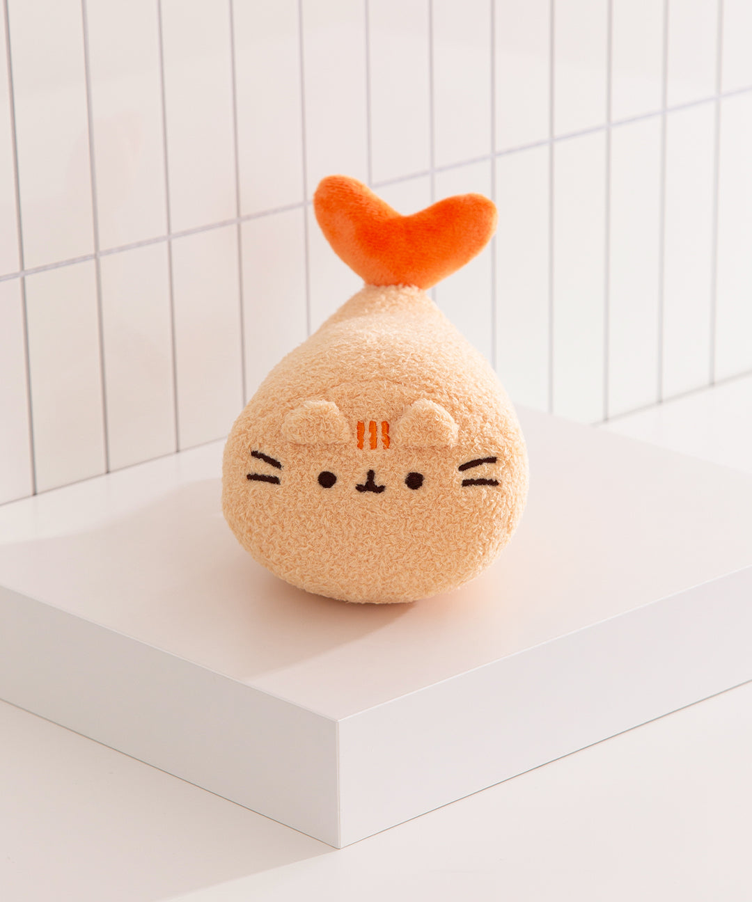 Plush toy shaped like a cat with an orange tail on a white surface