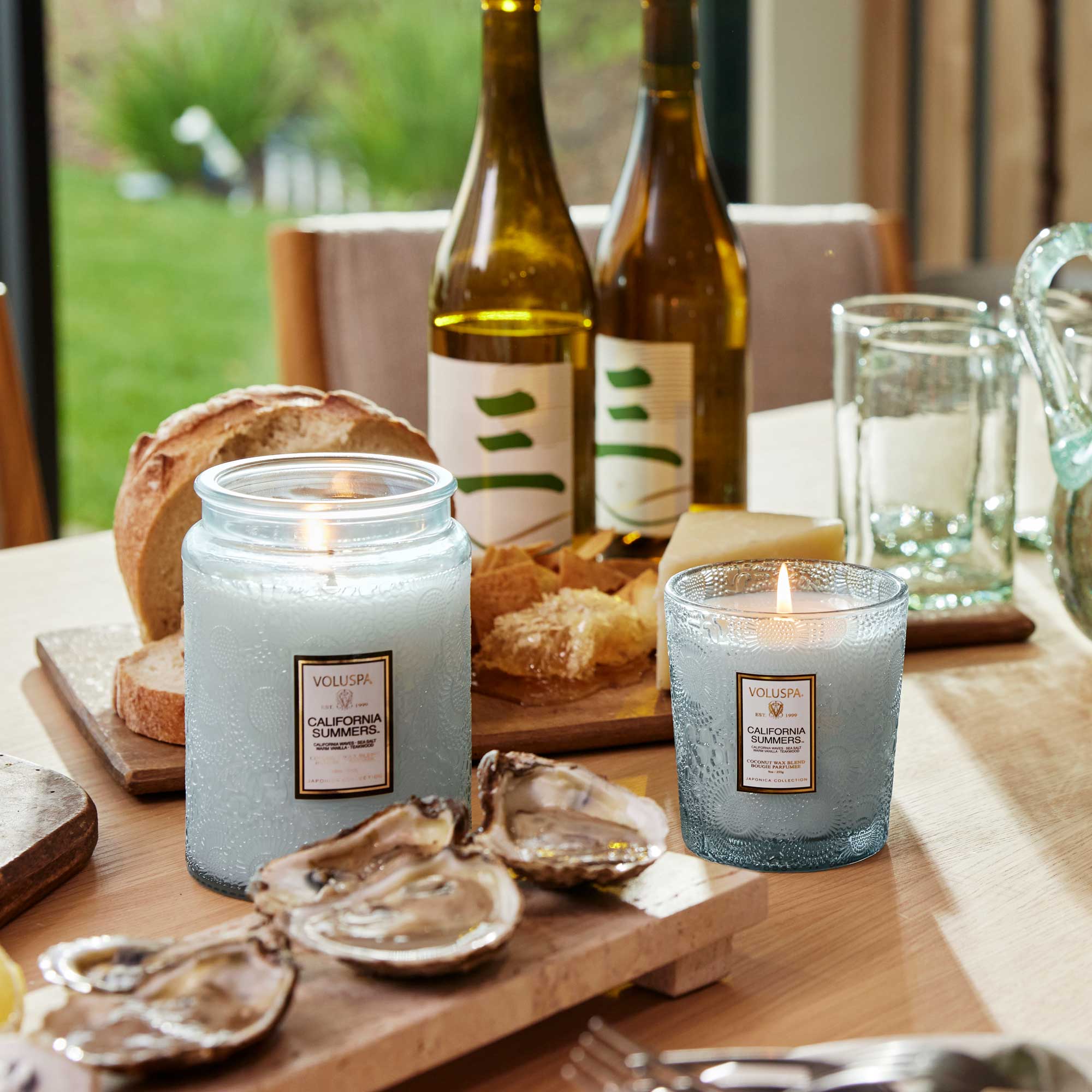Two candles on a table with bread, wine, and oysters