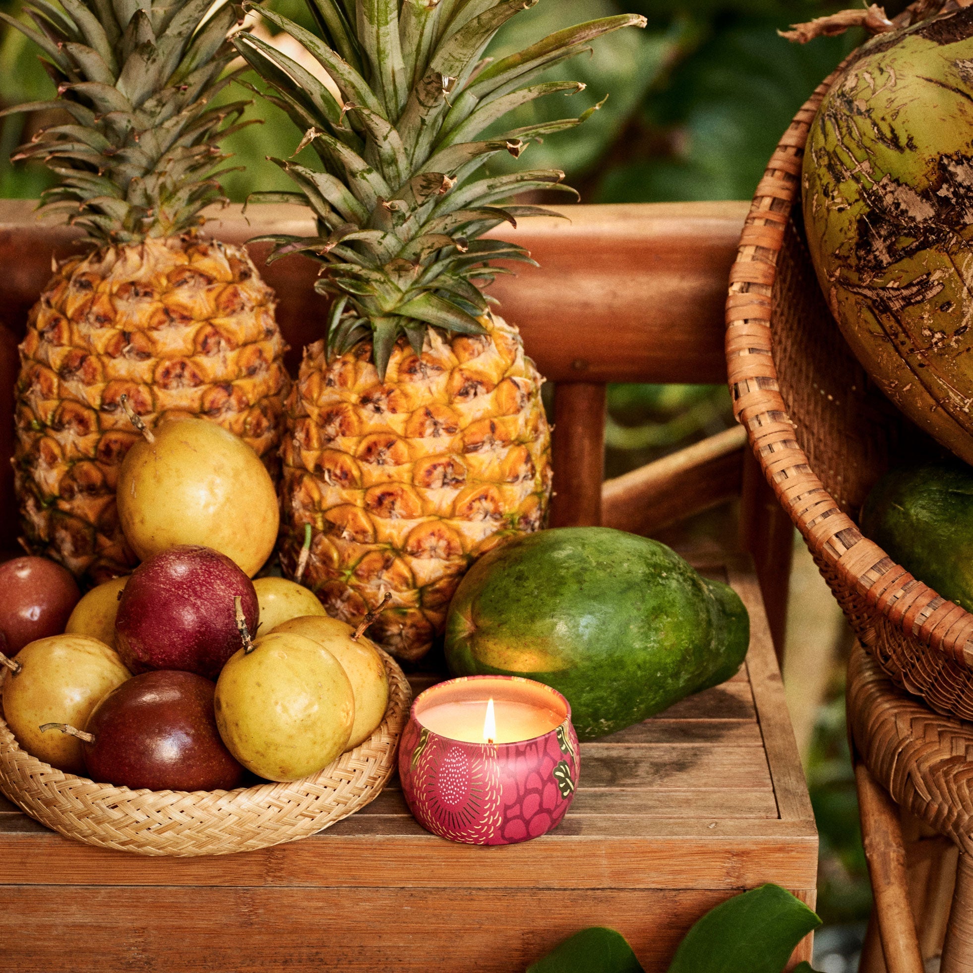 Fruit basket with pineapples, apples, and a candle on a wooden surface.