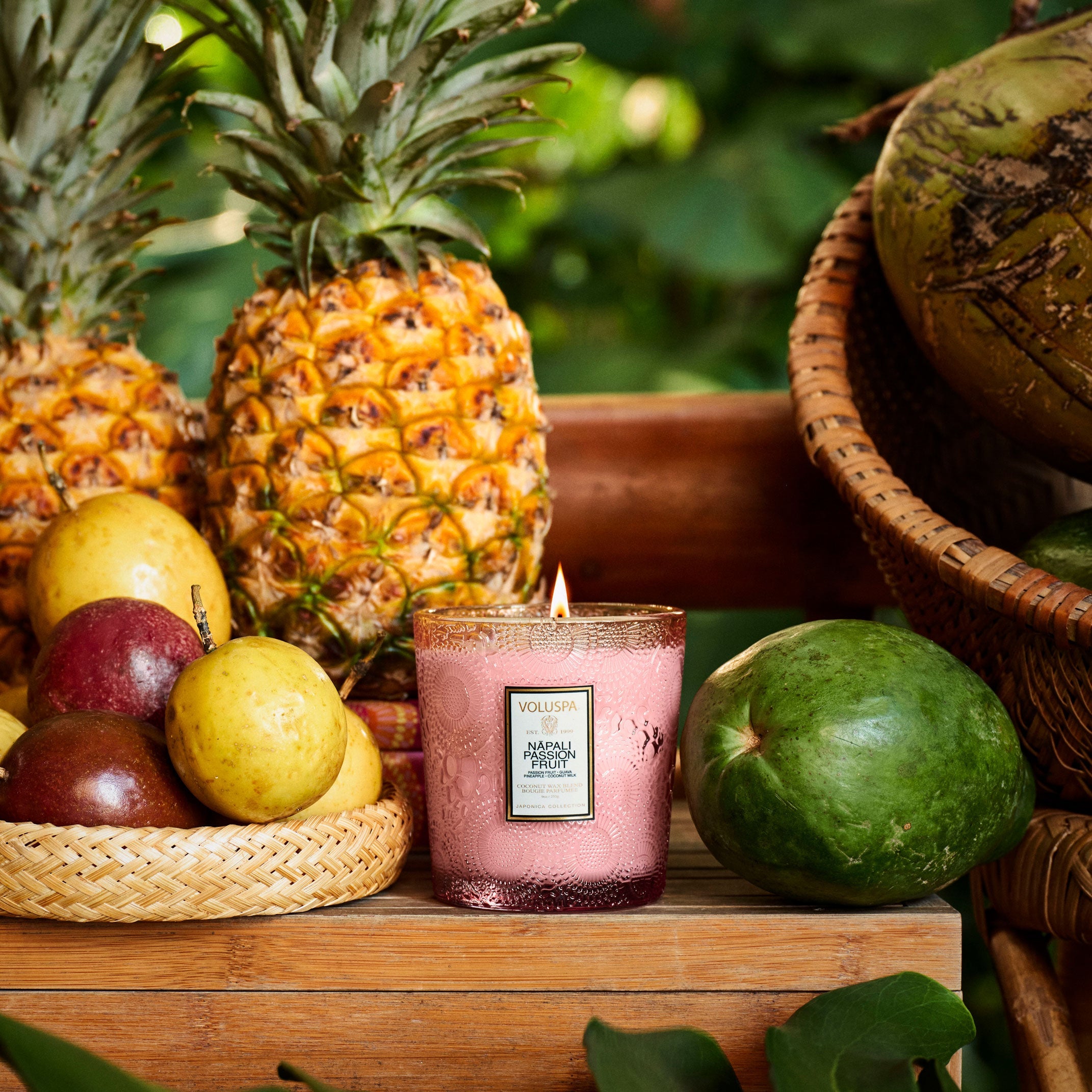 Candle with a pineapple and fruit display on a wooden surface