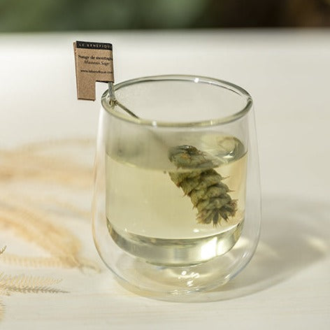 Glass of tea with a sprig of sage steeping inside and a small paper label.