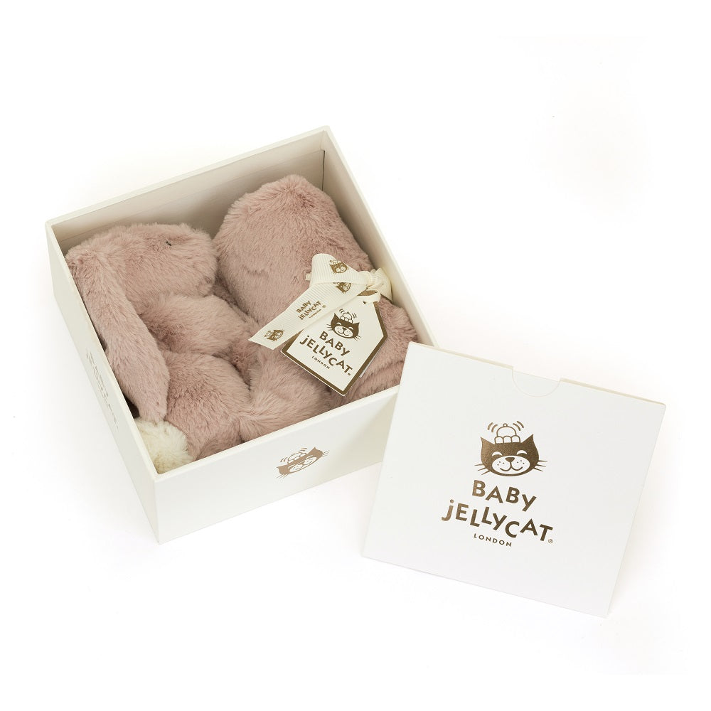 Product shot of a blush pink Baby Jellycat bunny toy inside an open white box, with the box lid next to it.