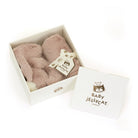 Product shot of a blush pink Baby Jellycat bunny toy inside an open white box, with the box lid next to it.