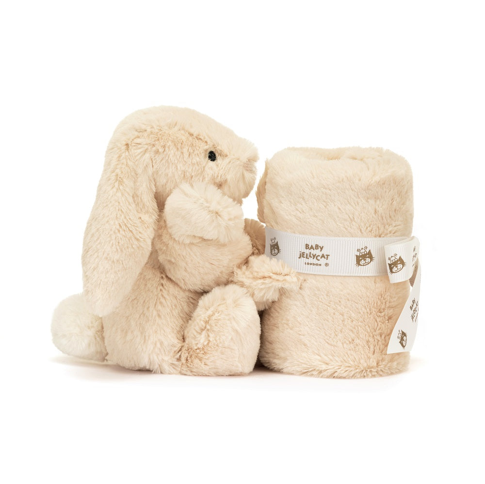 Beige plush bunny toy sitting next to a rolled-up blanket with a Baby Jellycat ribbon around it.