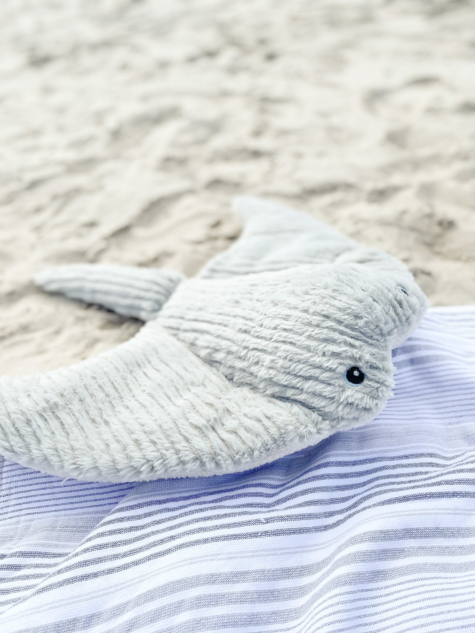 Stuffed gray shark toy on blue striped towel, beach background.