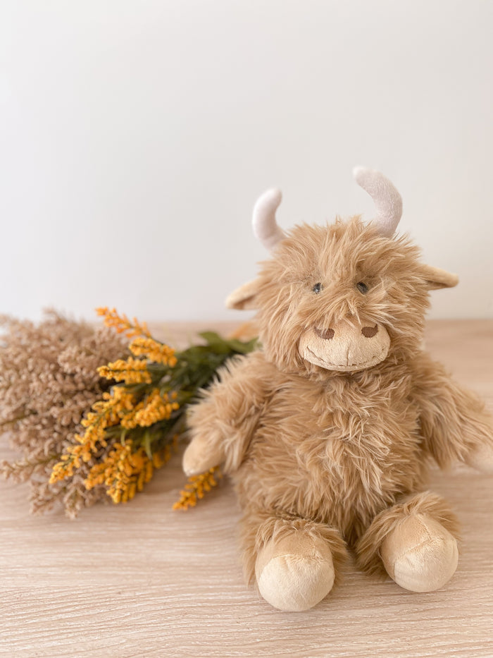 Plush toy cow with horns on a wooden surface with dried flowers and leaves.