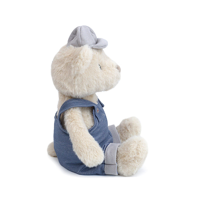 Stuffed teddy bear wearing denim overalls and a gray cap.