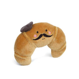Here are a few descriptive alt tags for the image, focusing on different aspects:
*   **Concise:** Plush croissant toy with mustache and beret.
*   **Descriptive:** Cartoonish brown plush croissant wearing a black beret and sporting a black mustache, on a white background.
*   **Emphasis on Character:** Stuffed croissant character with a mustache and beret.