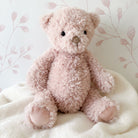 Pink fluffy teddy bear sitting on a white blanket.