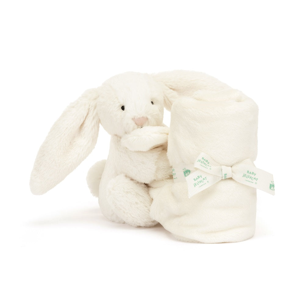White plush bunny holding rolled white blanket with ribbon.