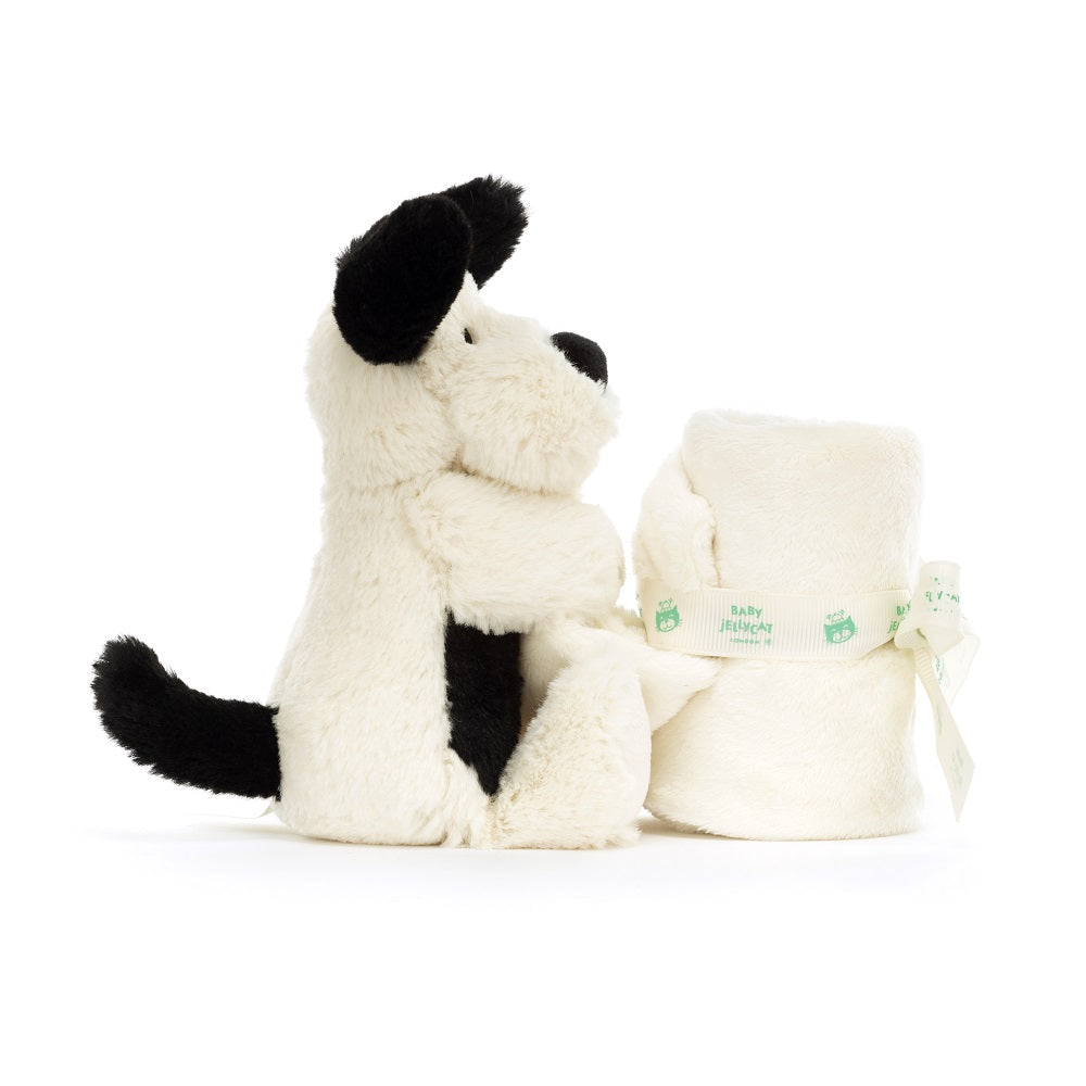 Stuffed cream-colored dog with black spots, next to a rolled-up blanket tied with a ribbon.