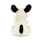 Rear view of a cream-colored stuffed dog with black ears and a black spot on its back.