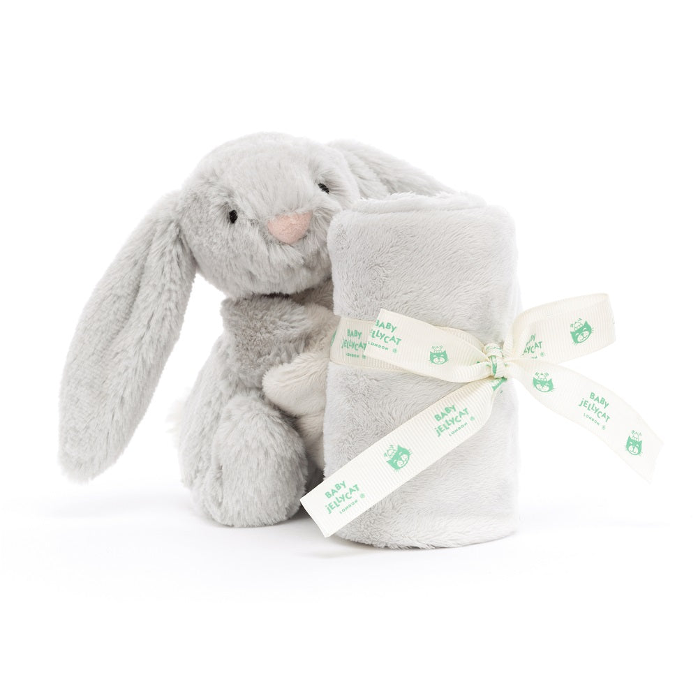 A gray plush bunny next to a rolled-up blanket, tied with a ribbon.