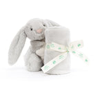A gray plush bunny next to a rolled-up blanket, tied with a ribbon.