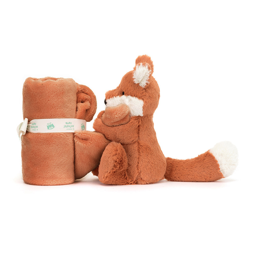 Stuffed orange fox sitting next to rolled orange baby blanket.