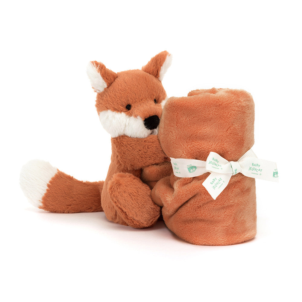 A plush toy fox sitting next to a rolled-up blanket tied with a ribbon.
