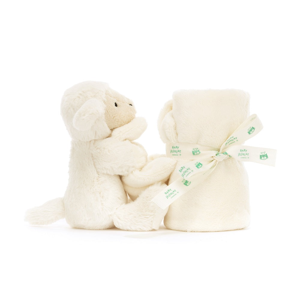 A white lamb stuffed animal next to a rolled blanket with a ribbon around it.
