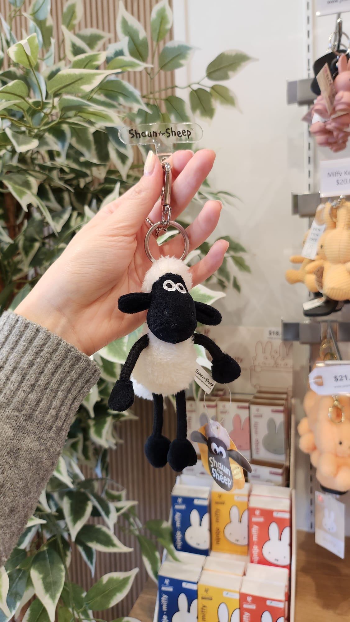 A plush "Shaun the Sheep" keychain is held up in front of a display of Miffy merchandise.