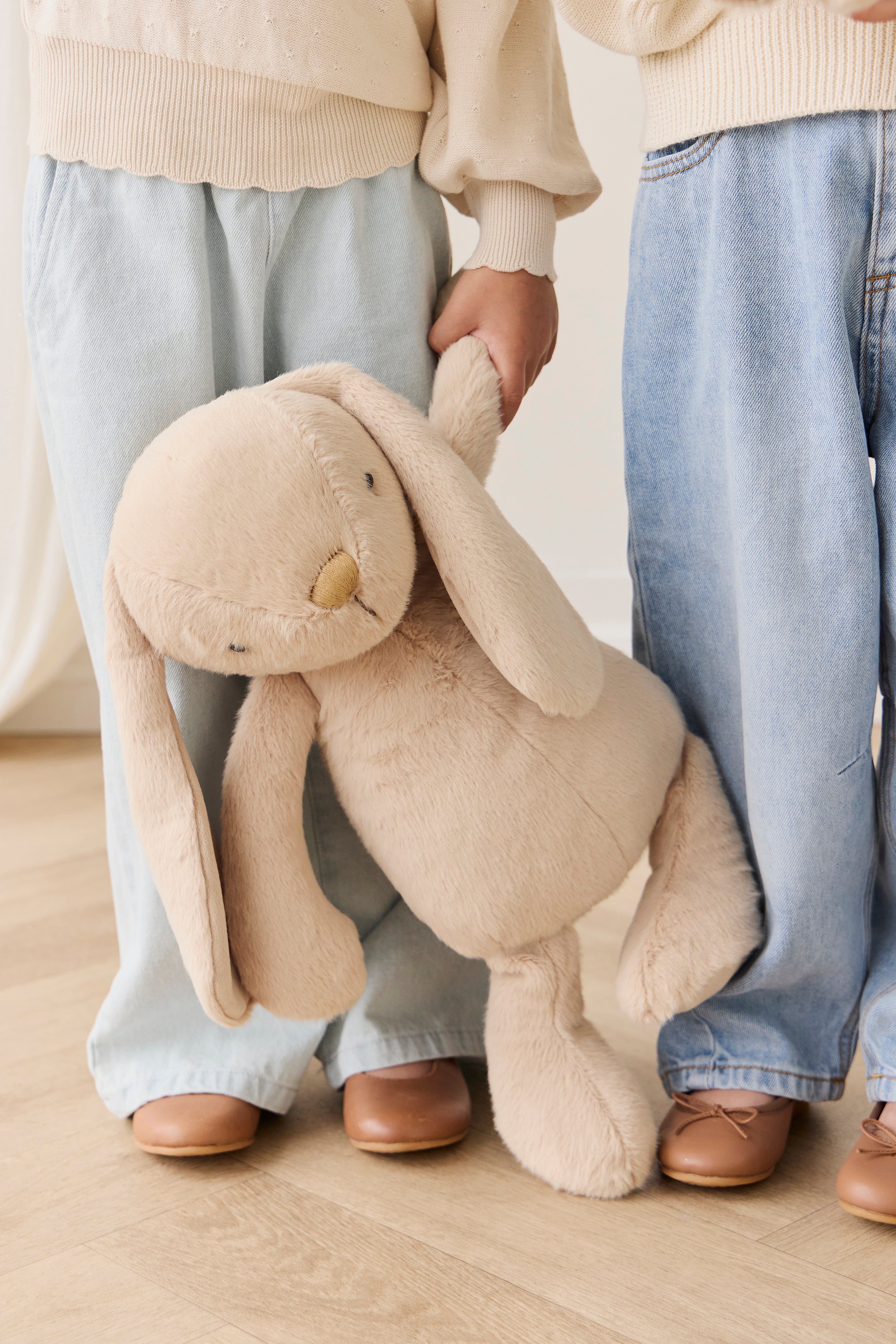 Person holding a large beige plush bunny toy on a wooden floor.