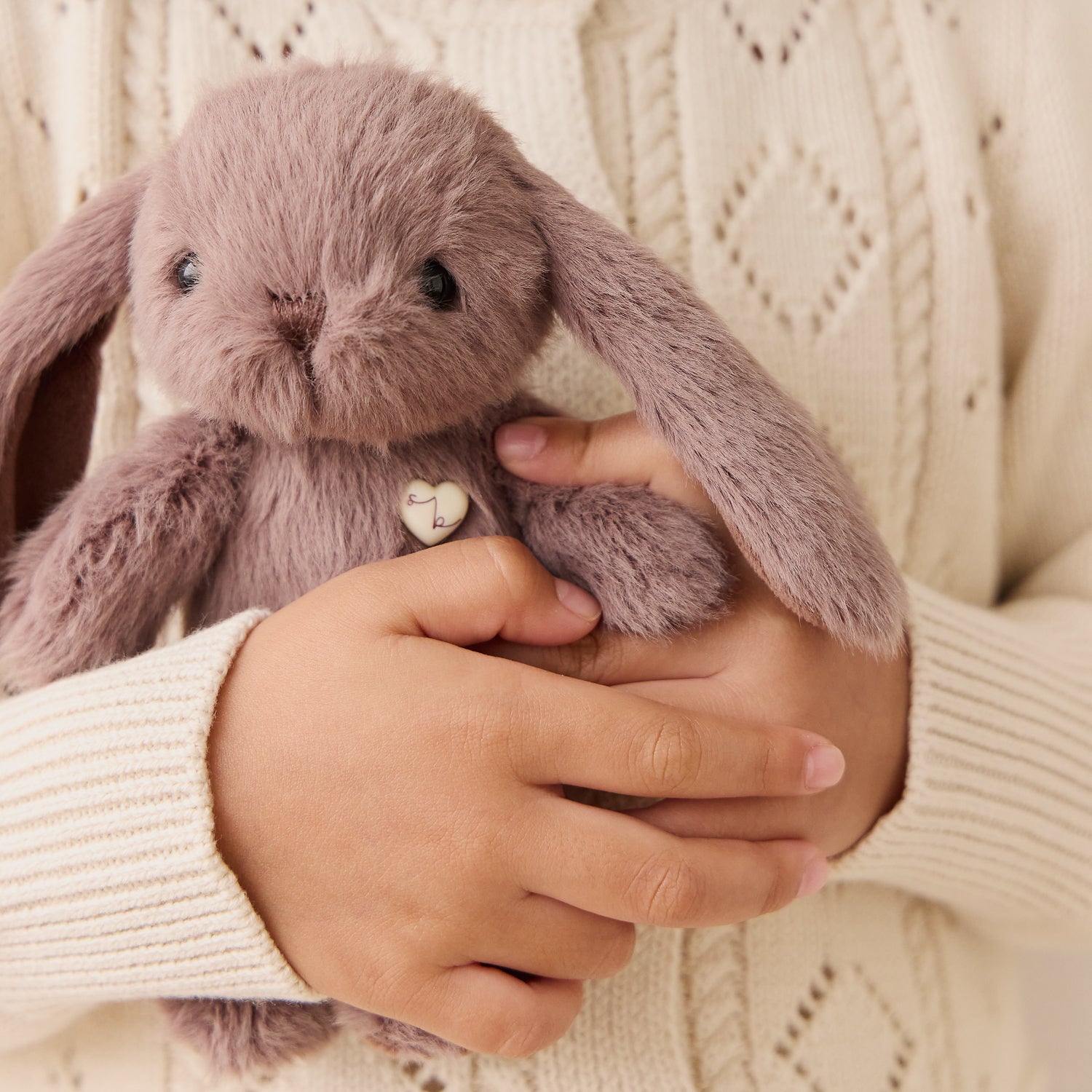 Person holding a plush bunny toy with a heart tag against a beige sweater background