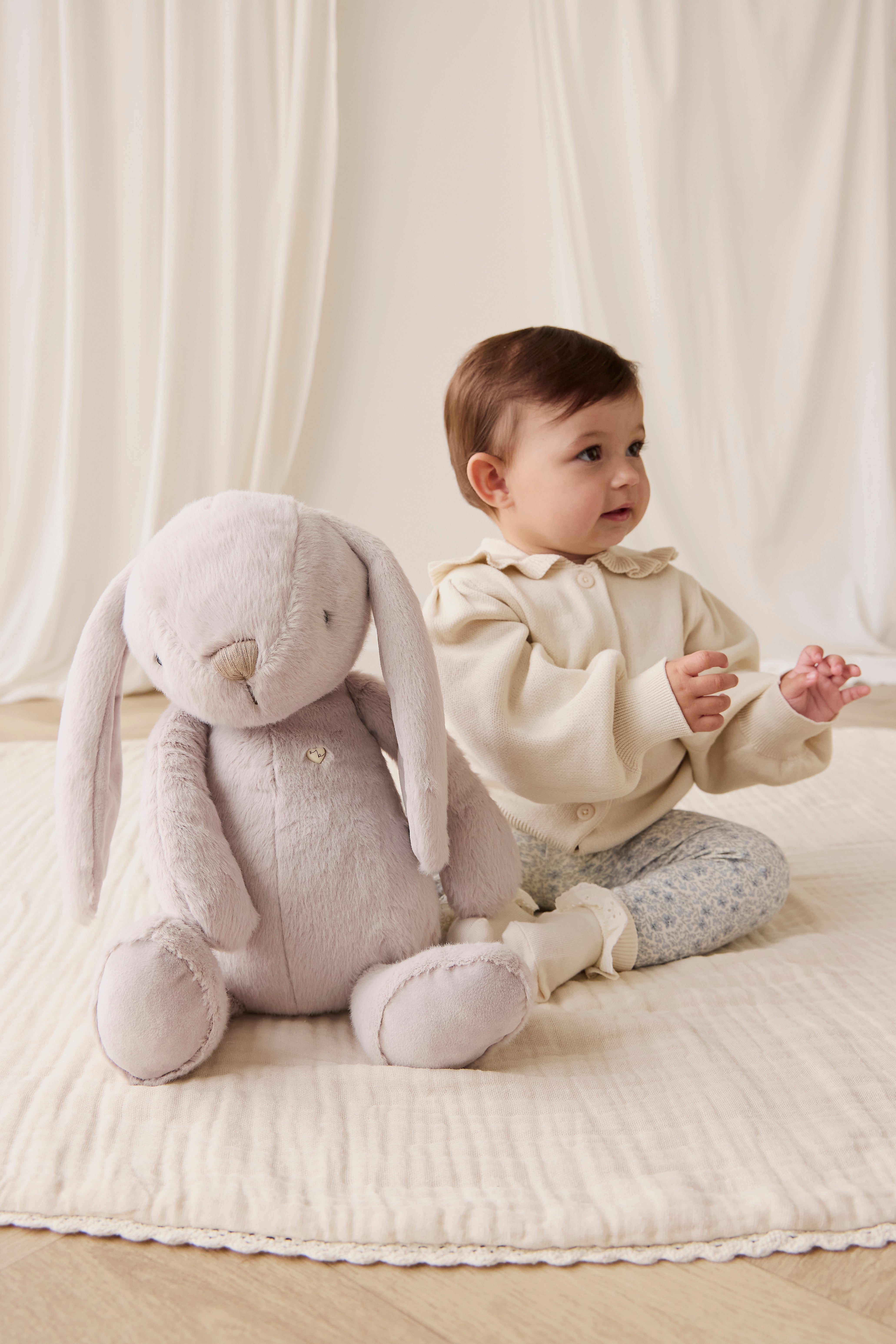 Baby sitting next to a plush rabbit toy on a soft surface