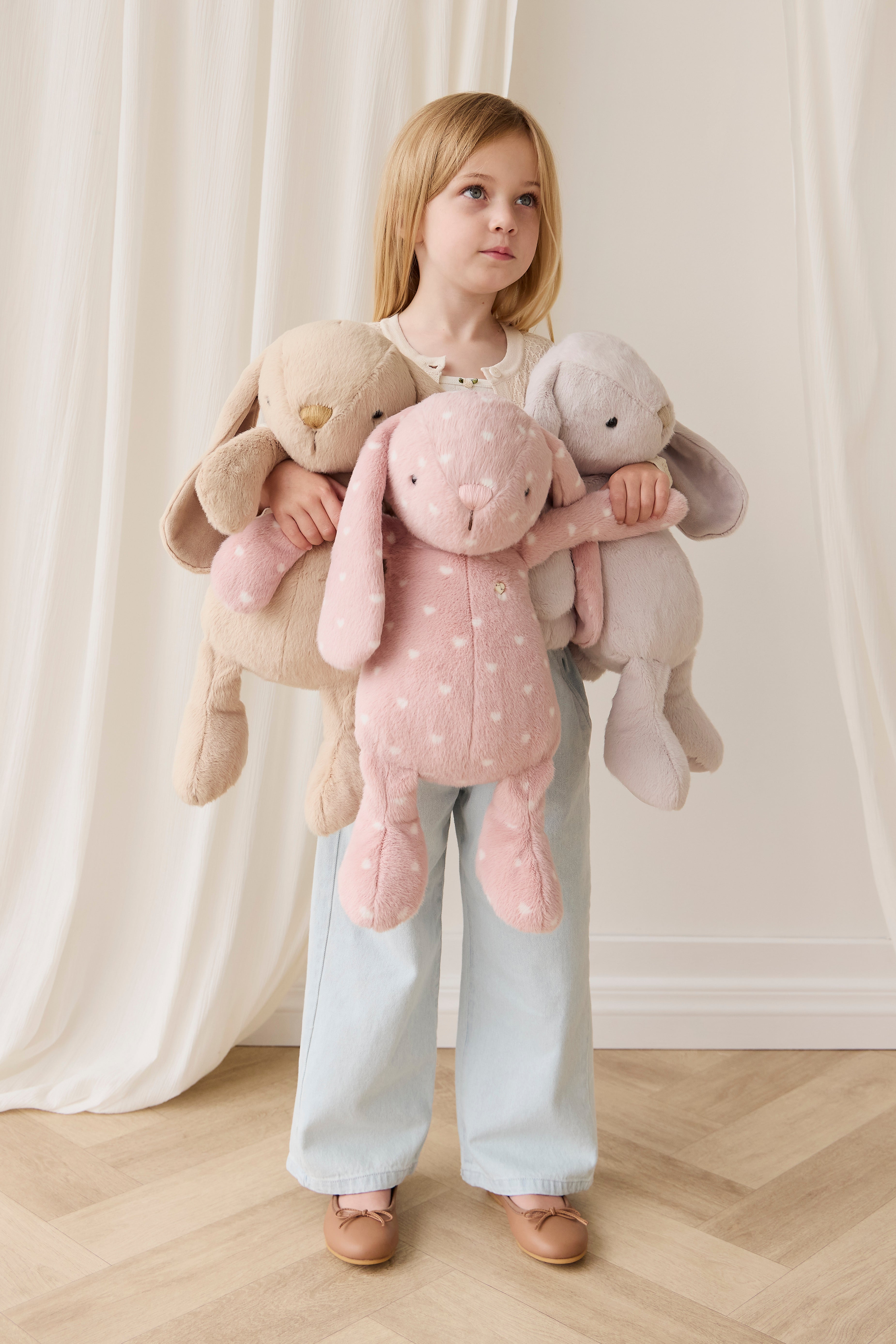 Child holding three plush toys against a white curtain background