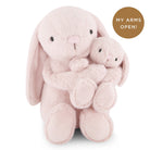Two light pink stuffed bunny toys, one hugging the other, against a white background.