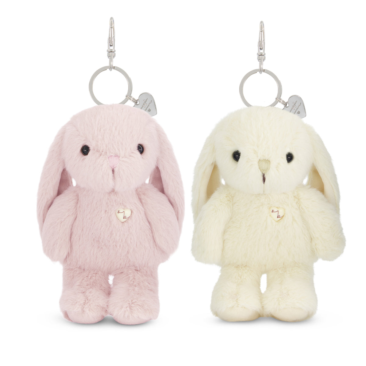 Two plush bunny keychains on a white background, one light pink and one cream/off-white, each with long floppy ears, small black eyes, a tiny stitched nose, and a small heart-shaped charm on a silver ring.