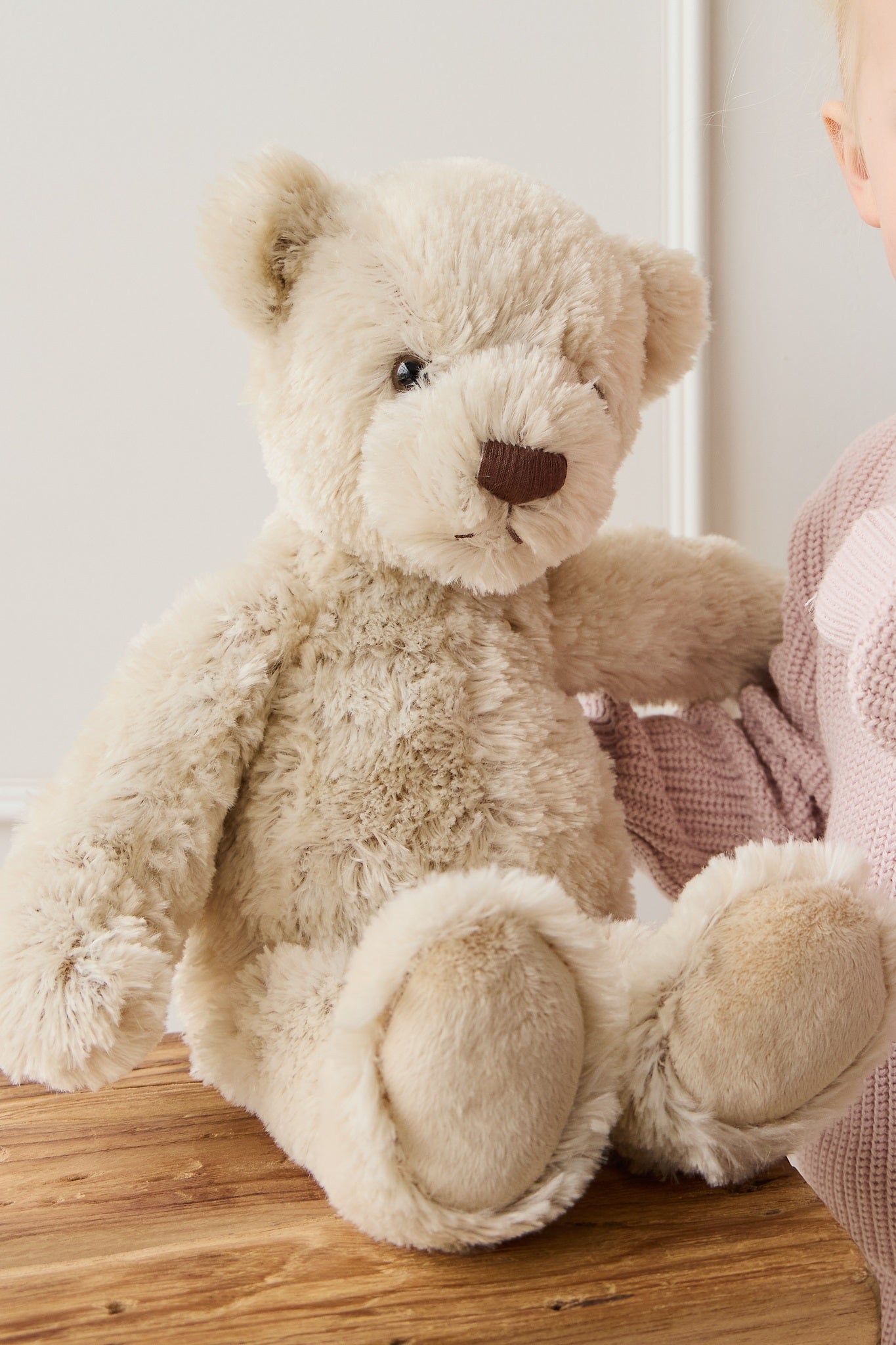 Tan plush teddy bear sitting on a wooden surface.