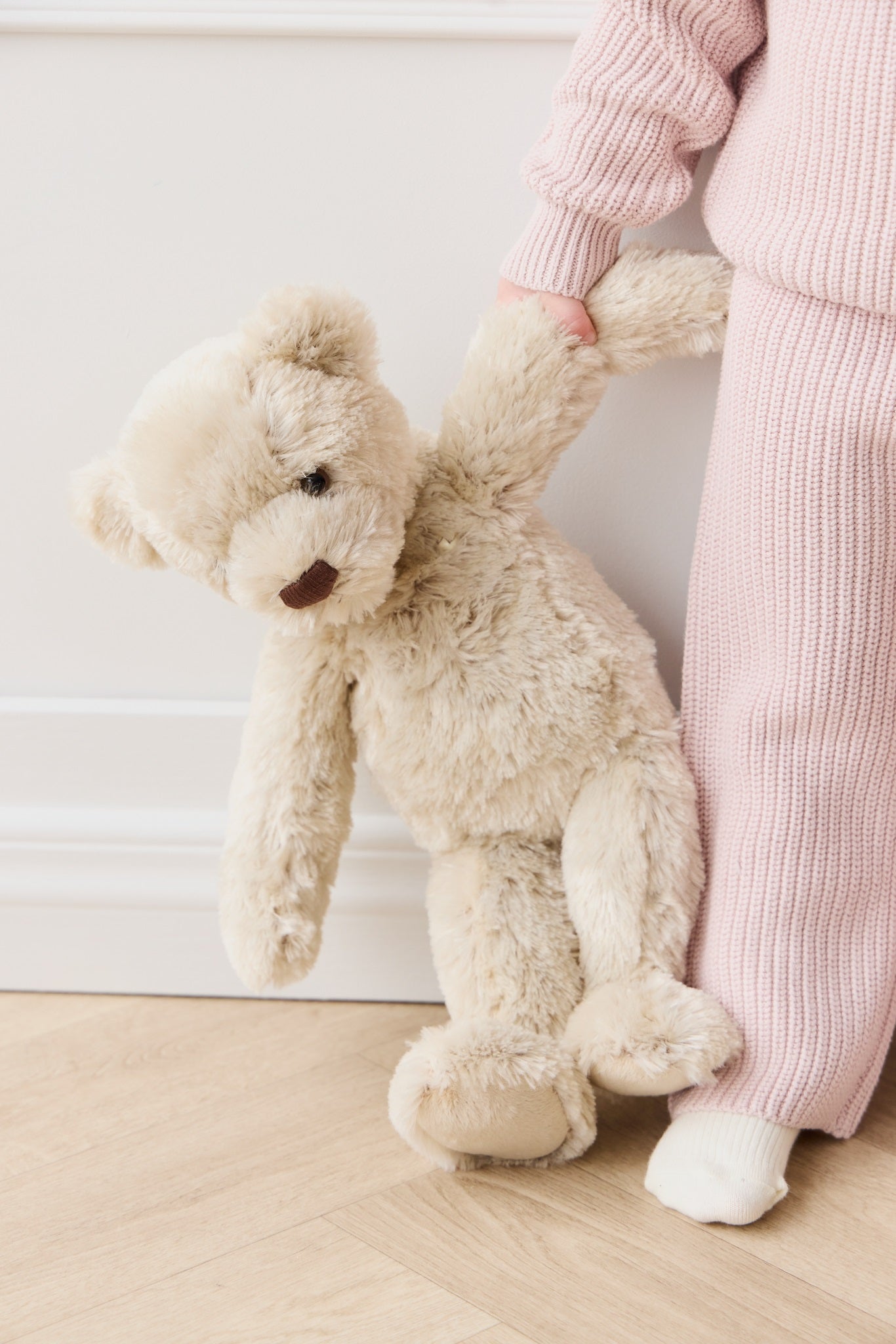 Child in pink knit suit holding a beige teddy bear.