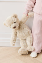 Child in pink knit suit holding a beige teddy bear.