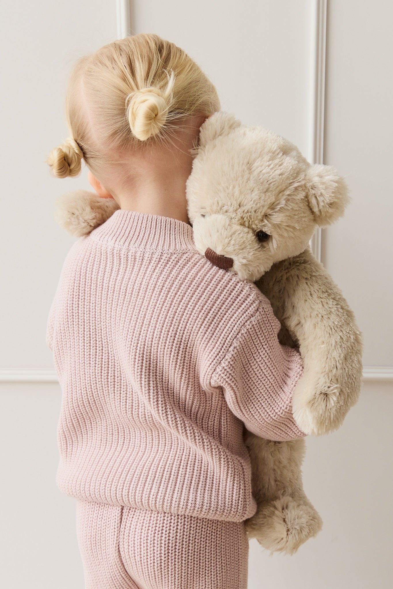 Child hugging teddy bear wearing a pink knit outfit.