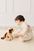Baby in knit outfit interacting with a plush dog toy on a neutral surface.