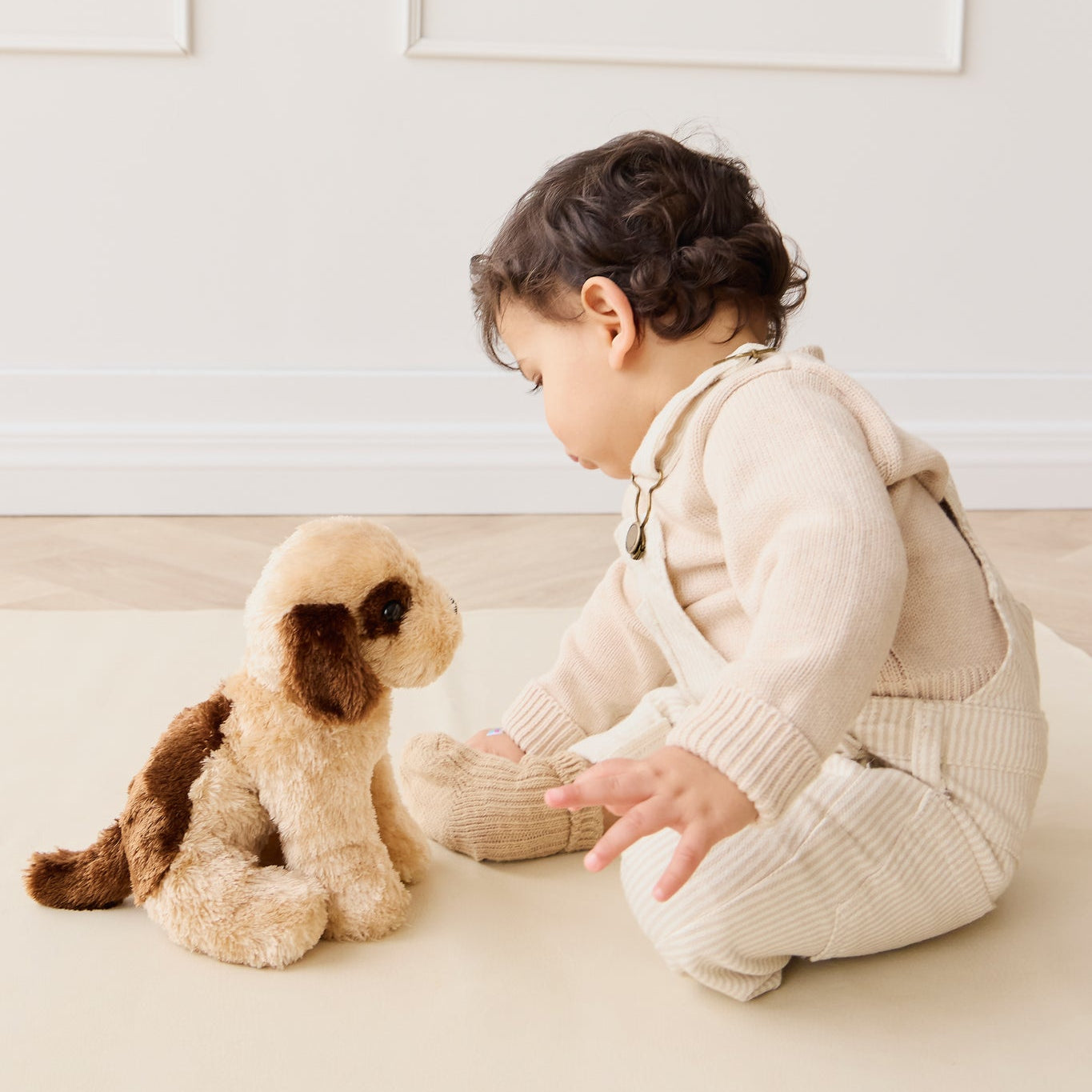 Baby in knit outfit interacting with a plush dog toy on a neutral surface.