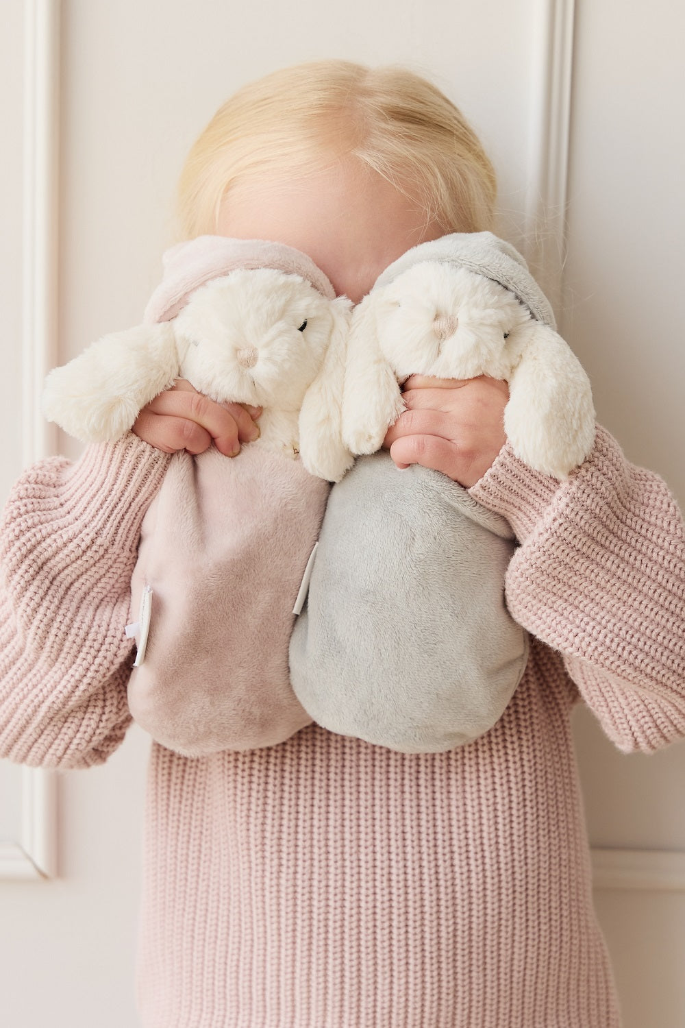Child holding two stuffed bunny comfort toys. Child wears a pink knit sweater.