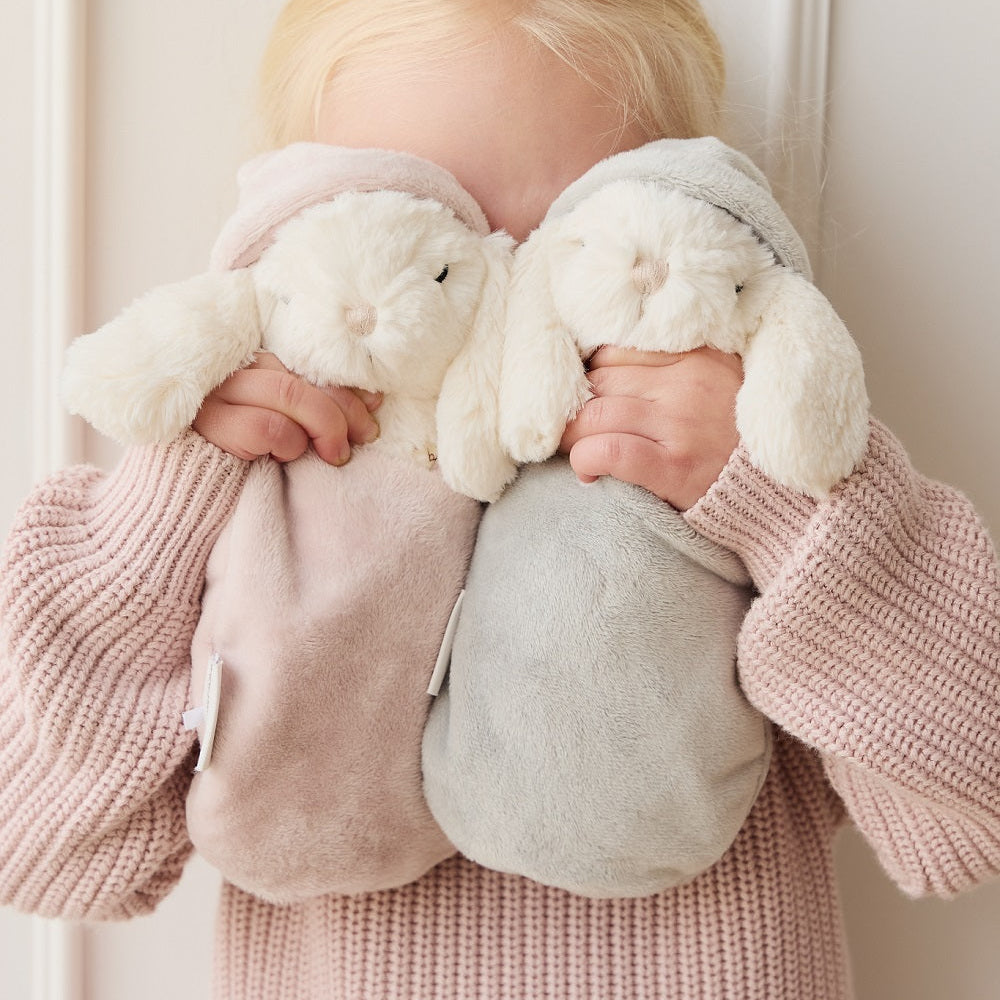 Child holding two stuffed bunny comfort toys. Child wears a pink knit sweater.