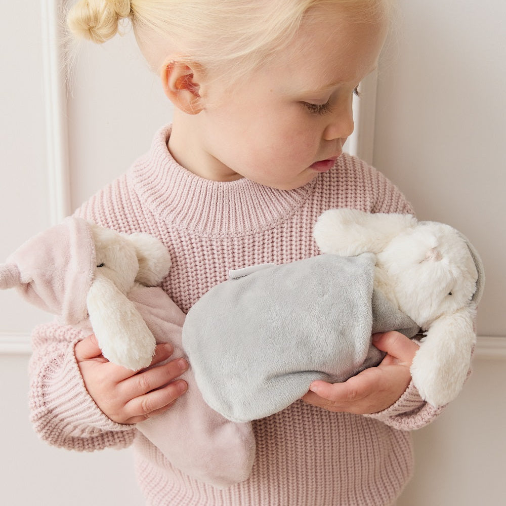 A young girl in a pink knit sweater holding two plush toys.