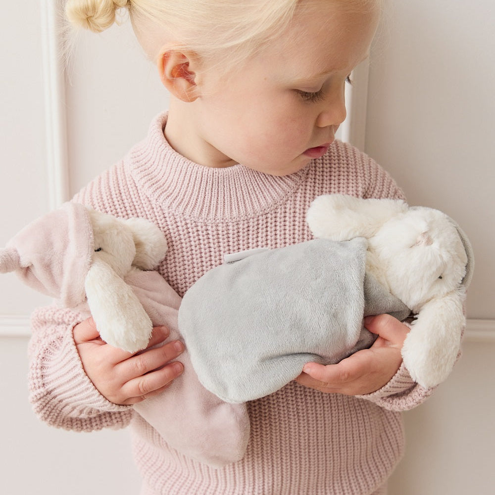 Blonde child holding two plush toys in pink knitwear.