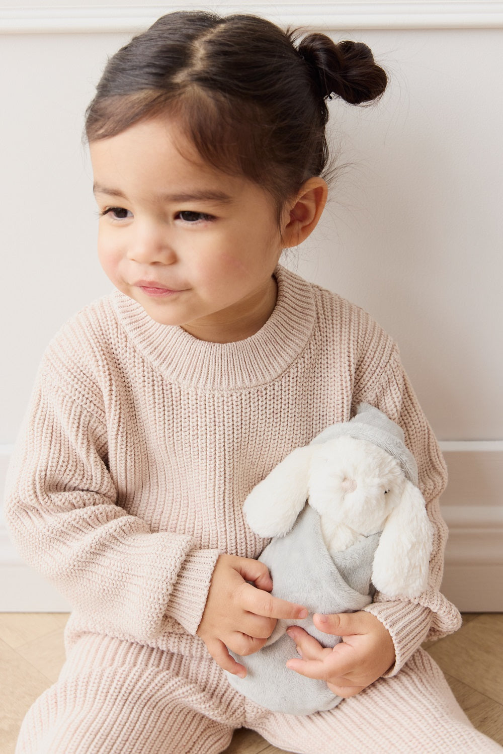 Young child in light pink knit outfit holding a stuffed bunny.