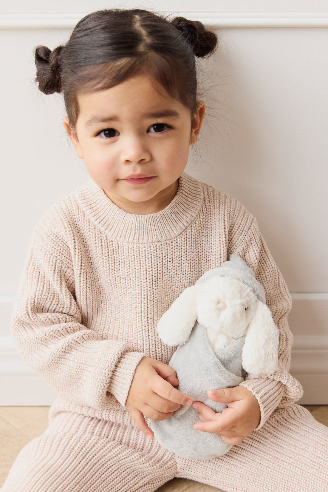 Toddler girl in knitwear holding a plush bunny.
