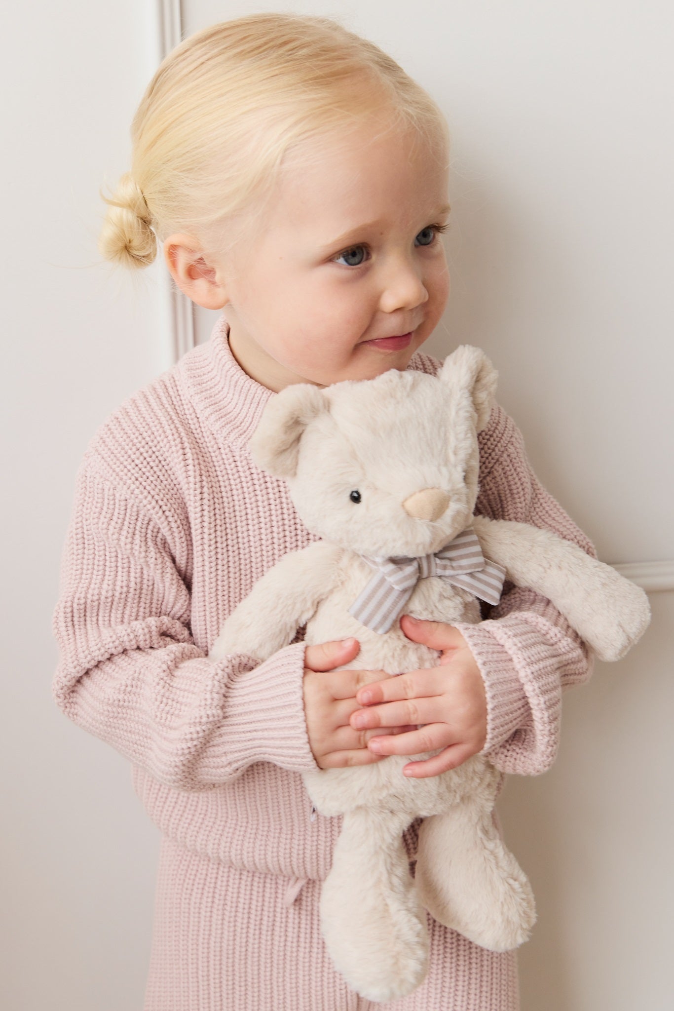 Little girl hugging a plush teddy bear wearing a pink knit sweater.