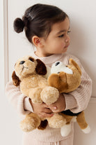 A young child in a pink knit sweater holding two plush dog toys.