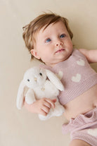 Baby in pink knit outfit holding a white plush bunny toy.