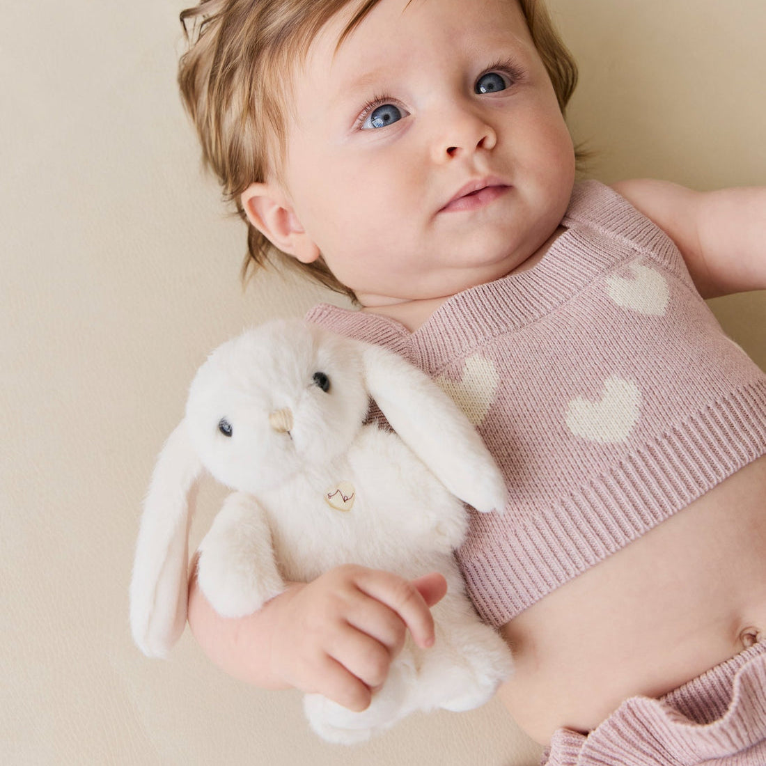 Baby in pink knit outfit holding a white plush bunny toy.